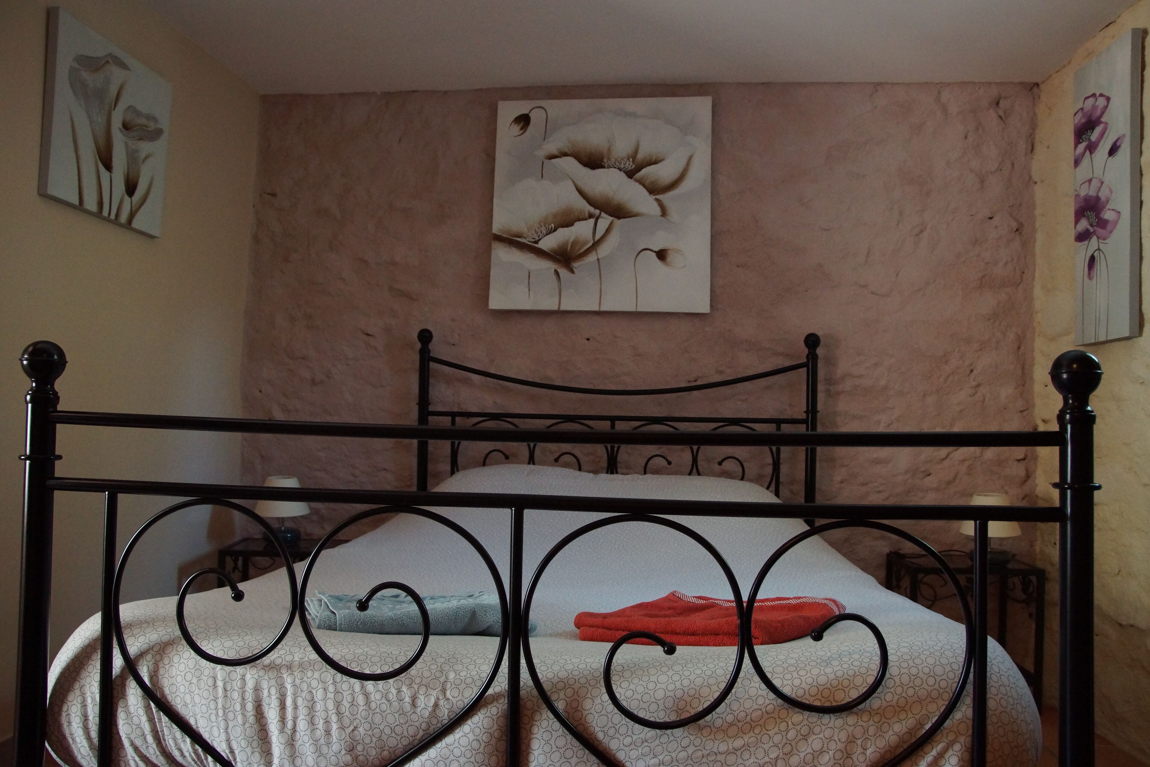 A bed with a metal frame, a wall with a floral painting, and a textured wall.