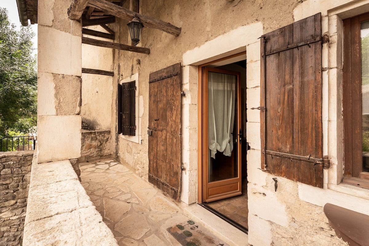 A rustic stone building with wooden shutters, a stone pathway, and a wooden bench.