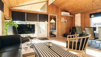 Una sala de estar moderna con televisor grande, techo de madera y un comedor con sillas y mesa.
