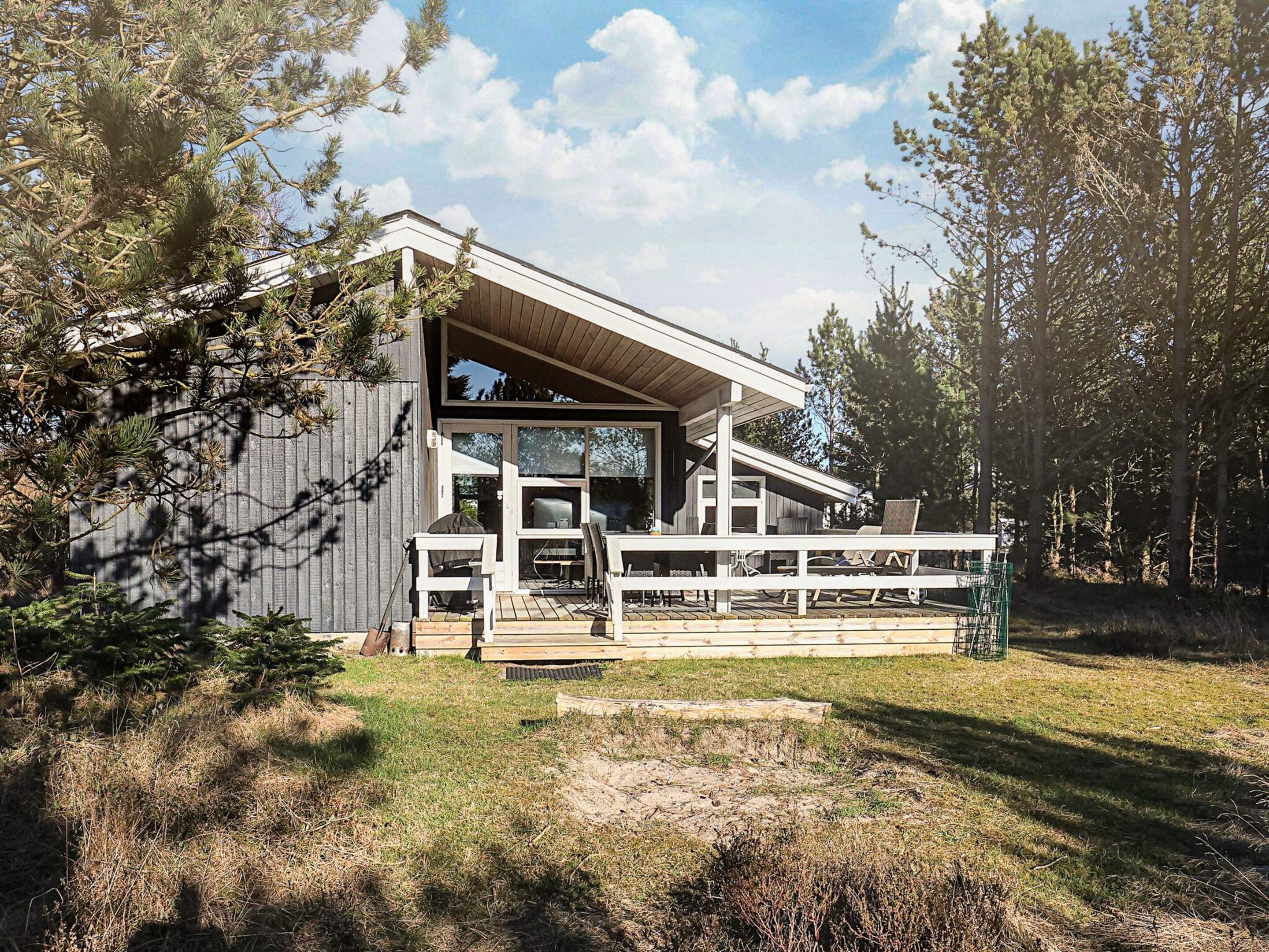 A modern house with a covered porch and a deck, surrounded by trees.