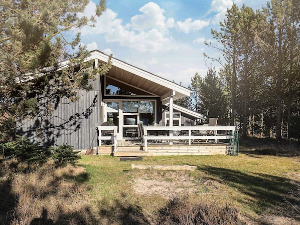 A modern house with a covered porch and a deck, surrounded by trees.