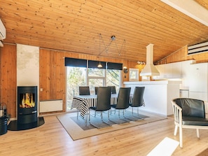 A cozy cabin interior with a wooden ceiling, a fireplace, a dining area with chairs, and a kitchen with white cabinets. - 4 Star Holiday Home in Albaek (Aalbaek)
