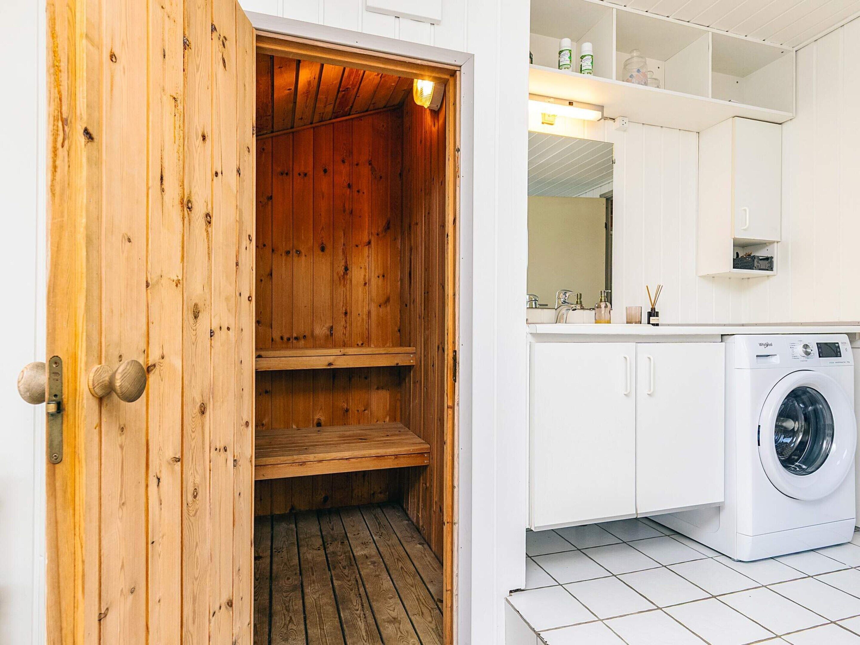 Una sala de lavandería con una lavadora, estantes de madera y suelo de baldosas blancas.