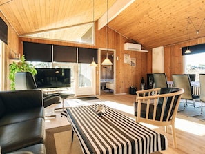 A modern interior with a wooden ceiling, a large window, a sofa, a dining area with chairs, and a television.