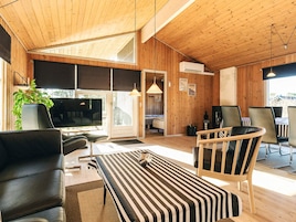 Un interior moderno con techo de madera, un ventanal grande, un sofá, un comedor con sillas y un televisor.