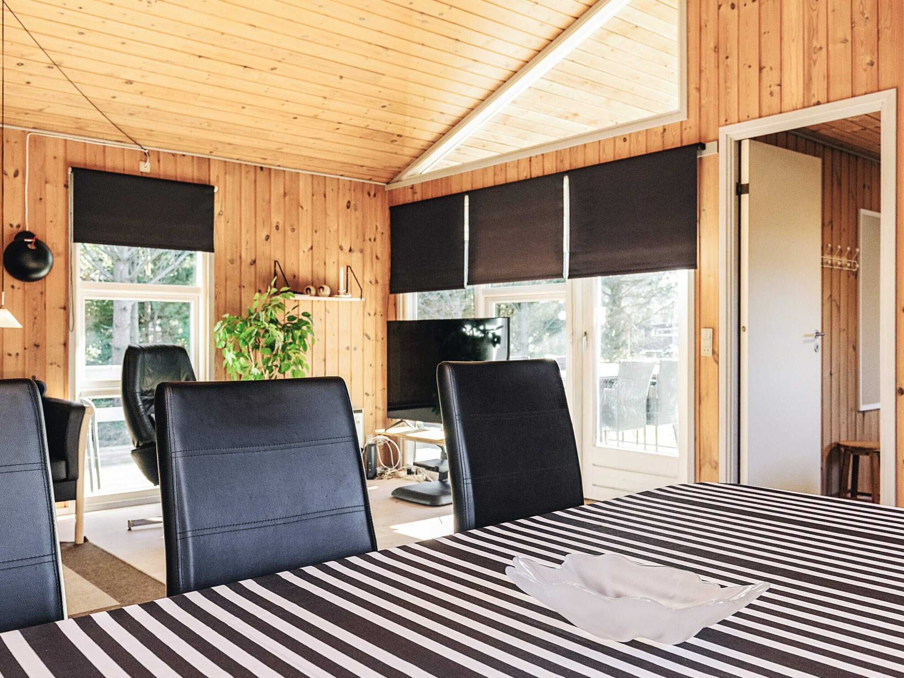 Una habitación con paredes de madera, una mesa a rayas negras y blancas y sillas negras.