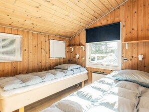 Une cabane avec deux lits superposés, des murs en bois, une fenêtre donnant sur un paysage agréable et un plafond avec des poutres apparentes.