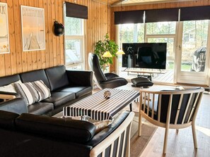 Un salon moderne avec un canapé en cuir noir, un pouf à rayures, une table basse en bois et un téléviseur.