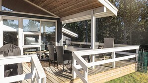 An outdoor deck with a wooden table and chairs, a grill, and a covered area with large windows. - 4 Star Holiday Home in Albaek (Aalbaek)