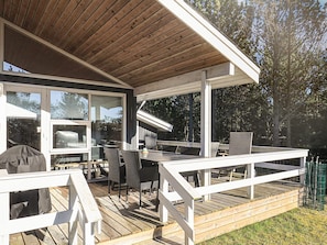 An outdoor deck with a wooden table and chairs, a grill, and a covered area with large windows. - 4 Star Holiday Home in Albaek (Aalbaek)