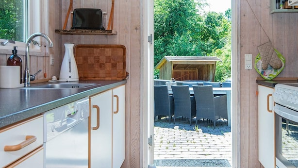 Ett kompakt kök med träskåp, en inbyggd mikrovågsugn och en liten matplats med sittplatser utomhus.