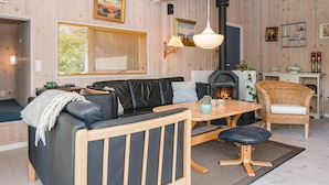 Ett mysigt vardagsrum med en öppen spis, en soffa, ett matbord och en fåtölj i rotting.