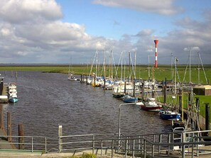 A marina with boats docked, a lighthouse, and a grassy area in the background.