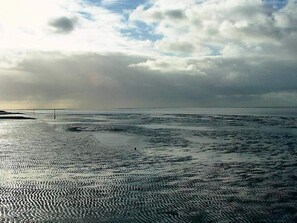 Una spiaggia con disegni sulla sabbia bagnata, un cielo nuvoloso e un orizzonte lontano.