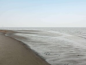 A beach with wet sand and gentle waves, a distant lighthouse, and a clear sky.