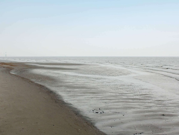 A beach with wet sand and gentle waves, a distant lighthouse, and a clear sky. - Holiday Home in Otterndorf (Otterndorf)