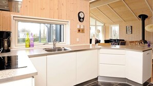 A modern kitchen with a large island, wooden walls, and a black clock on the wall. - Modern Cottage With Spa - By Traum Ferienwohnungen (Sjølund)