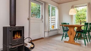 Una habitación acogedora con una estufa de leña, una mesa de comedor con sillas y grandes ventanales con cortinas.
