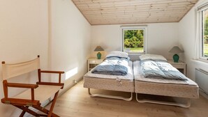 Un dormitorio pequeño con dos camas individuales, techo de madera, ventana con vista a zonas verdes y una silla de madera.