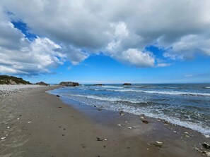 A beach with a clear sky, calm sea, and rocky outcrops.