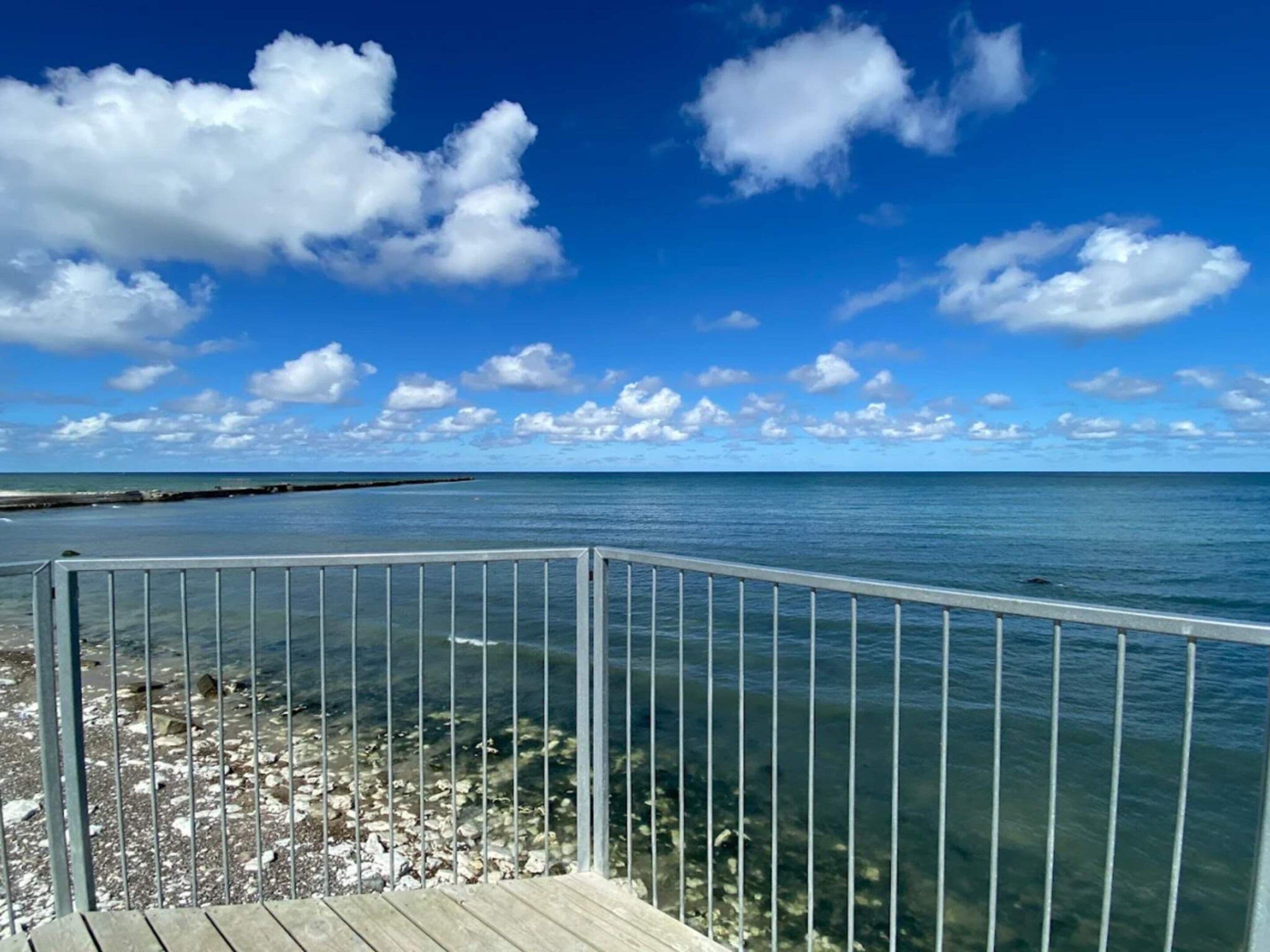 Vista despejada del océano desde una terraza de madera con barandilla de metal.