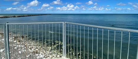 A clear view of the ocean from a wooden deck with a metal railing.