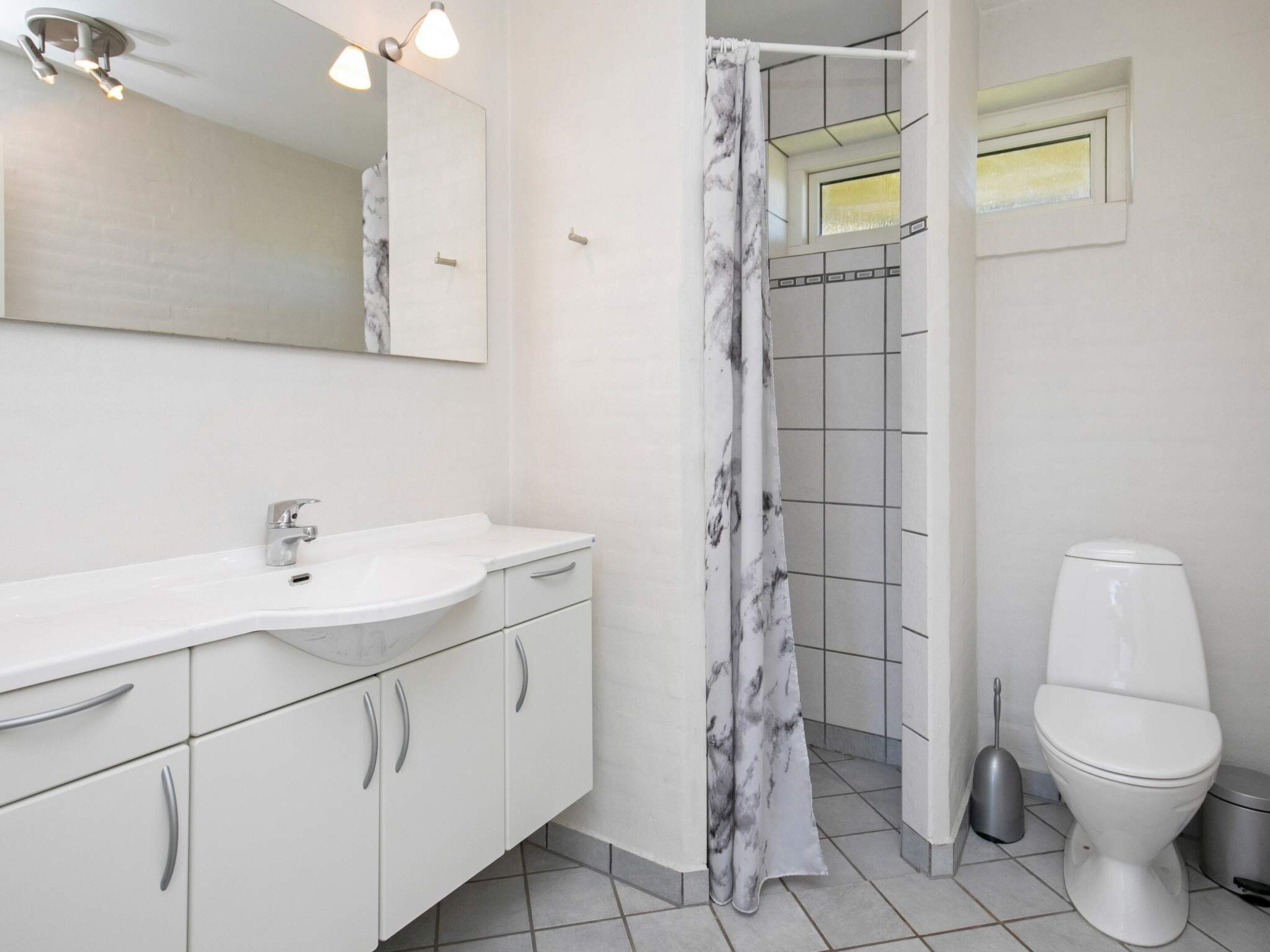 Un baño con lavamanos, espejo y retrete blancos.