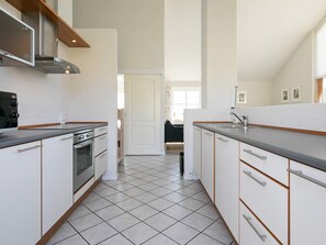 A modern kitchen with white cabinetry, a stainless steel range hood, and a tiled floor. - 4 Star Holiday Home in Hanstholm (Hanstholm)
