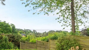 Une terrasse en bois offrant une vue sur un jardin luxuriant et sur une étendue d’eau lointaine.