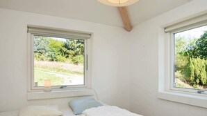 Une chambre avec deux fenêtres, un lit avec une literie blanche et une table de chevet avec une lampe.