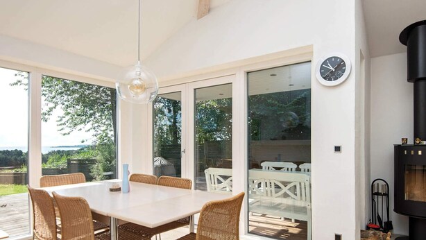 Un espace repas moderne avec une grande table et des chaises en osier, un luminaire suspendu et une cheminée.