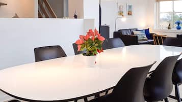 Uma área de refeições moderna com uma mesa branca, cadeiras pretas e um vaso com flores vermelhas.