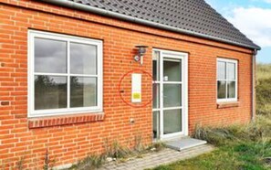 A red brick building with a tiled roof, a door with a glass panel, and a window with a white frame.