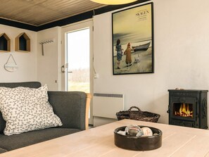 En hyggelig stue med sofa, pejs, et indrammet kunstværk og et vindue.