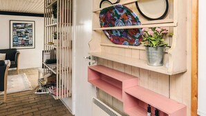 A room with a wooden wall, a colorful abstract painting, a metal bucket with flowers, and a framed photo on the wall.