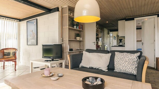A living room with a sofa, a TV, a table with a bowl of stones, and a pendant light.