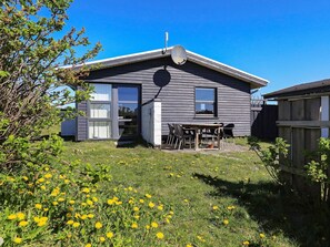 A house with a satellite dish, a patio with chairs, and a garden with yellow flowers.