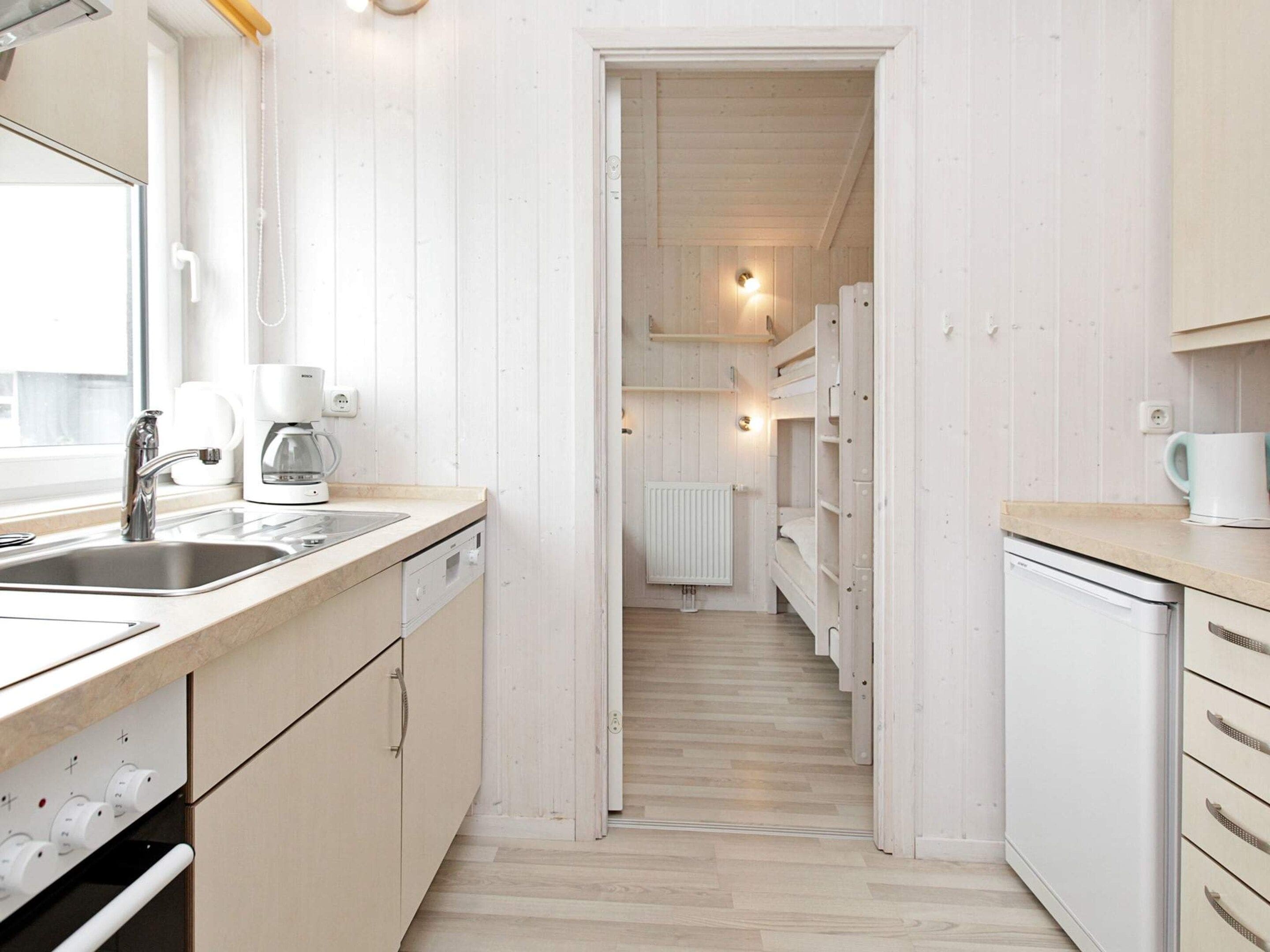 Cocina pequeña con un lavamanos, cafetera y vista a un dormitorio con literas.