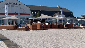 A beachside building named Strandhalle with outdoor seating areas and flags.