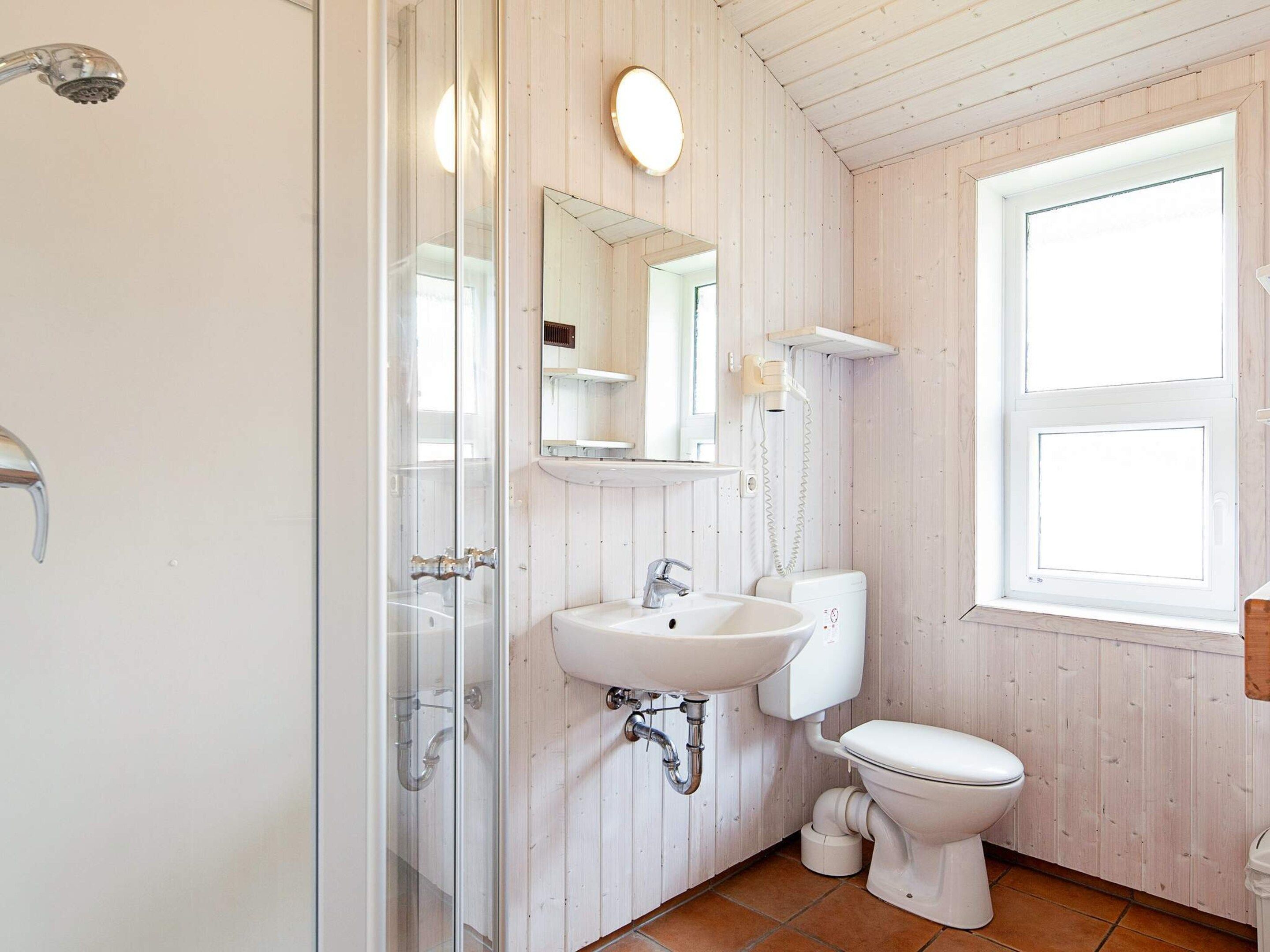 A bathroom with a shower, sink, toilet, and a window.