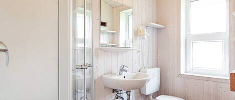 A bathroom with a shower, sink, toilet, and a window.