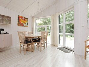 Ein Essbereich mit einem Holztisch, Stühlen, einem Bild an der Wand und großen, mit Vorhängen drapierten Fenstern.