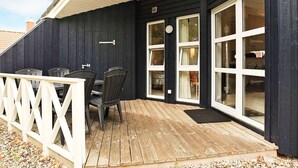 Una terraza con mobiliario exterior, piso de madera y barandilla blanca.