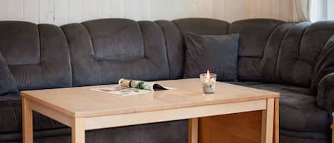 A living room with a dark brown sectional sofa, a wooden coffee table, and a small glass candle holder.