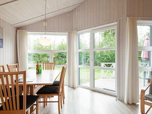 A dining area with a wooden table and chairs, large windows, and a view of greenery outside. - Holiday Home in GrÃ¶mmitz (Groemitz)