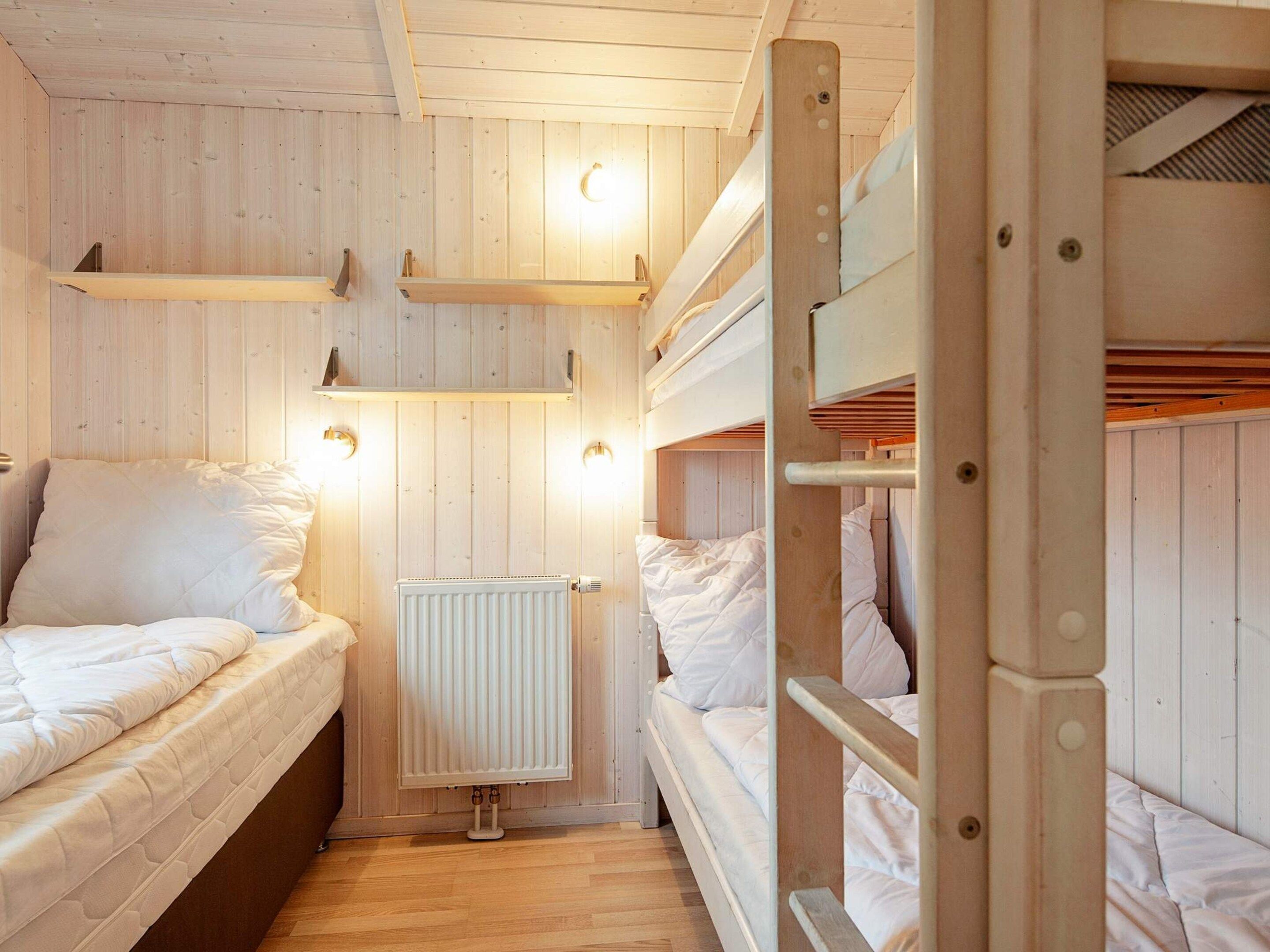 Ein kleines Zimmer mit Etagenbetten, einem Heizkörper und Wandleuchten.