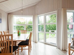 A dining area with a wooden table and chairs, large windows with curtains, and a view of greenery outside. - Holiday Home in GrÃ¶mmitz (Groemitz)