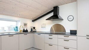 A modern kitchen with white cabinets, a black range hood, a sink, and a clock on the wall. - 4 Person Holiday Home in Borkop-by Traum (Borkop)