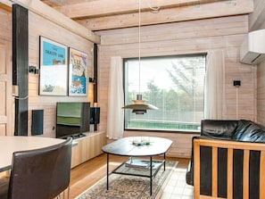 A cozy room with a wooden ceiling, a dining table with chairs, a sofa, a TV, and a window with blinds.