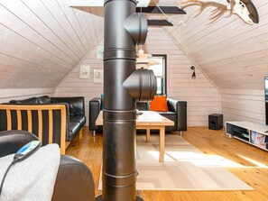 Een gezellig zolderkamertje met een schuine kap, houten wanden, een zwarte leren bank, een houten tafel en een boekenplank.